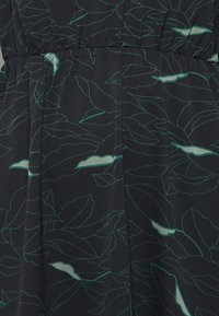 Gros plan sur un tissu foncé avec des motifs de feuilles bleu sarcelle et vert clair et un détail froncé élastique.
