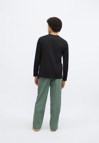 Cămașă neagră cu mânecă lungă, asortată cu pantaloni verzi cu carouri. Cămașa are un design simplu, în timp ce pantalonii prezintă un imprimeu texturat.