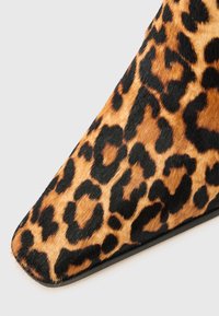 Chaussure à talon haut en imprimé léopard avec un bout pointu, fabriquée dans un matériau en fausse fourrure texturé et dotée d'une semelle noire. Accents de taches brunes et noires.
