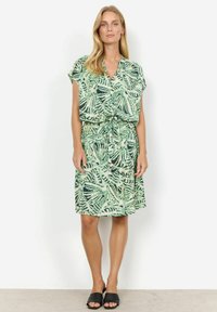 Kortsleeve, omslagskjole i lys grøn med botanisk print. Har elastisk talje og en afslappet silhuet. Sorte slidesandaler.