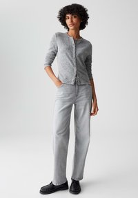 Gray knitted cardigan with button closure, long sleeves; paired with light gray straight-leg jeans and black shoes. Simple and textured design.