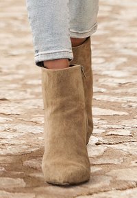 Béžové semišové kotníkové boty s kulatou špičkou a bočním zipem, kombinované se světle modrými, mírně roztrhanými skinny džíny.