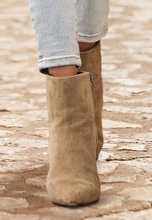 Bottines en suède beige avec un bout rond et une fermeture éclair sur le côté, associées à un jean skinny légèrement déchiré de couleur bleu clair.