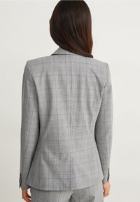 Chaqueta de traje a cuadros gris con un corte entallado, solapas de muesca y una abertura sencilla en la parte trasera, con líneas azules y negras en el patrón.