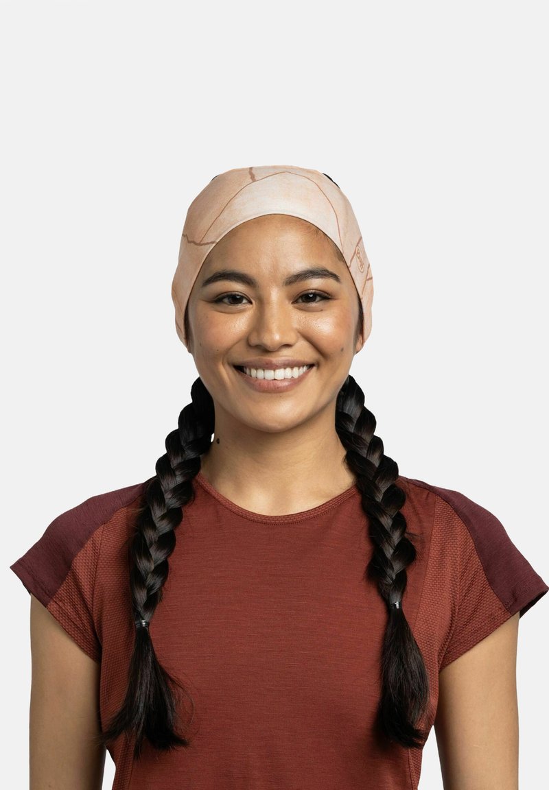 Cinta para la cabeza ligera con patrón en tonos durazno y textura suave; utilizada con una camiseta deportiva de manga corta en color óxido.