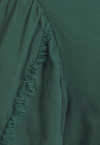 Tessuto verde scuro con un dettaglio arricciato lungo una cucitura, che mostra texture e design tessile a strati.