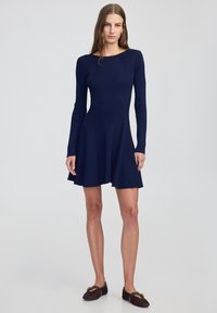 Marineblauw geribbelde gebreide jurk met lange mouwen, een aansluitende bustier en een uitlopende rok. Soepele textuur, ronde halslijn en eenvoudige silhouet.