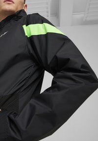 Zwarte blazer met een groene accentstreep, met een matte textuur, sportief ontwerp en mesh details aan de zoom.