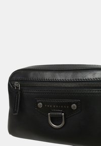 Borsa cosmetica nera in pelle con finitura testurizzata, chiusura con zip, patch frontale con logo e dettagli in metallo.