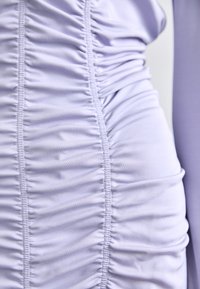 Light lavender dress featuring soft, stretchy fabric with vertical ruching and smooth texture. Ruched detailing adds dimension to the design.