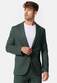 Dunkelgrüner Fischgrätblazer mit Reverskragen, Einfachknopfverschluss, zwei Vorder-taschen und strukturiertem Stoffdetail.