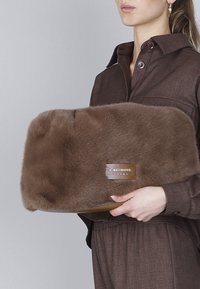 Bruine handtas van bont met een gladde textuur en rechthoekige vorm. Bevat een goudkleurige plaat met "Café Noir" ingegraveerd.