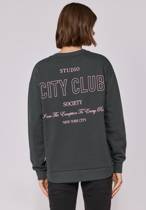 Sweatshirt vert foncé à coupe décontractée. Présente un texte rose : "CITY CLUB," "STUDIO," et "NEW YORK CITY." Poignets et ourlet côtelés.