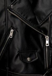 Černá bunda z umělé kůže s několika kovovými zipy a kapsou na druky. Texturovaný povrch a design s překrytým límcem.