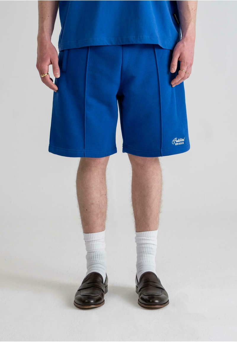 Shorts din fâșie albastră, cu o croială lejeră, având o tivire cusută și buzunare laterale. Asortați cu șosete albe și pantofi slip-on maro.