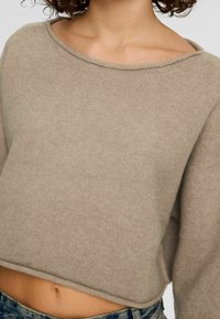 Beżowy krótki sweter wykonany z miękkiej dzianiny, z szerokim dekoltem i lekko teksturowany. Luźny fason, z widocznymi szwami na dole.
