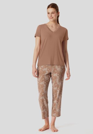 Braunes Kurzarm-V-Ausschnitt-Shirt kombiniert mit beigen gemusterten Hosen mit floralem Design. Das Material scheint weich und leicht zu sein.