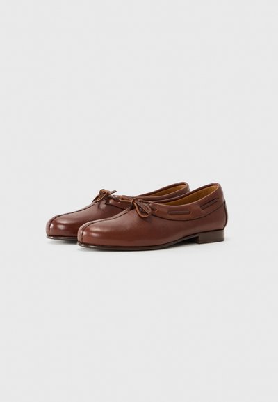 Zapatos de cuero marrón con punta redondeada, detalle de lazo y cortes laterales. Presentan un tacón bajo de madera y una textura suave.