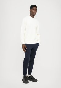 Sudadera blanca de manga larga con puños acanalados, combinada con pantalones navy ajustados. El calzado es negro, de textura suave y con cordones.