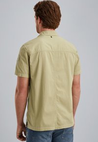 Short-sleeve, light green shirt in a casual design, featuring a straight hem and a subtle logo detail at the back neck.