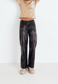 Svarta läderbyxor med avslappnad passform, med synliga söm detaljer och en lätt glänsande yta. Matchas med beige skor.