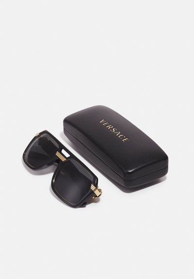 Occhiali da sole neri con design squadrato, dettagli dorati sulle aste e lenti scure, confezionati in un astuccio in pelle nera Versace con lettering dorato.