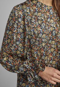 Blusa con stampa floreale e maniche lunghe a sbuffo; presenta uno sfondo blu navy e fiori multicolori. I polsini arricciati aggiungono texture.