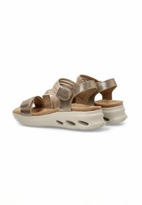 Sandalias metálicas doradas con una suave plantilla de color beige, correas elásticas y hebillas ajustables. Presentan una suela acolchada con respiraderos.