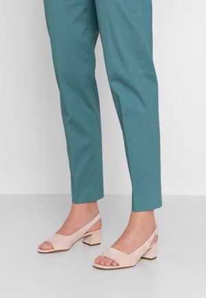 Jasnoróżowe zamszowe sandały na słupku z odkrytym palcem i cieniowanym wzorem; noszone z turkusowymi spodniami o dopasowanym kroju na jednolitym białym tle.