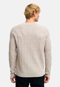 Sweter w warkocze w jasnym beżu, wykonany z wełny lub podobnego materiału. Posiada ribbowane mankiety i dół, z teksturowanym wzorem powierzchni.