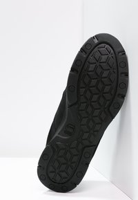 Suela de zapatilla atlética negra con una superficie texturizada, que presenta un patrón hexagonal y estrías para un mejor agarre. Diseño ligero y flexible.