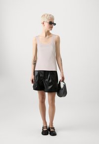 Lys rosa ribbet tanktop med firkantet utringning, kombinert med sorte faux skinn plisserte shorts. Tilbehør inkludert en liten mørk veske og solbriller.
