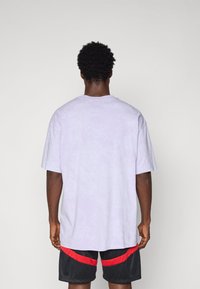 Lys lilla oversized t-shirt med rund hals og korte ærmer, parret med sorte shorts med røde striber. Blød bomuldsstruktur.