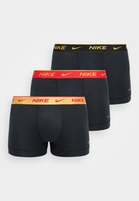 Tri páry čiernych boxeriek, ktoré majú elastické pásky v červenej, žltej a čiernej farbe. Každý pás má logo "Nike" v kontrastných farbách.