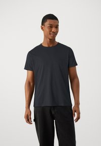 T-shirt preta de gola redonda feito de algodão macio, com mangas curtas e um corte descontraído, combinado com jeans escuros.