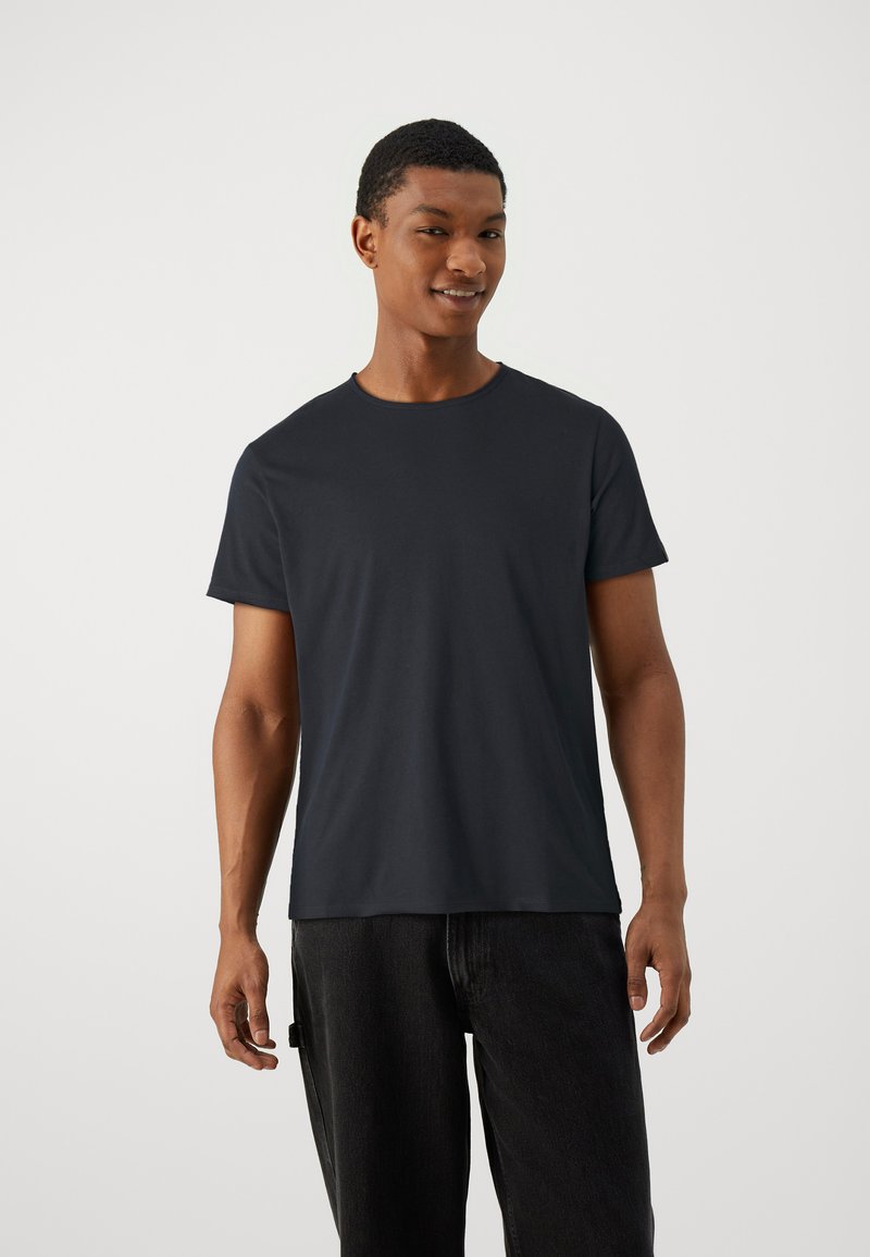 T-shirt preta de gola redonda feito de algodão macio, com mangas curtas e um corte descontraído, combinado com jeans escuros.