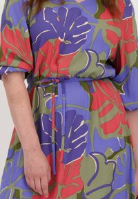 Bloemendess met paars, rood en groene kleuren. Gemaakt van een lichtgewicht stof met een ceintuur in de taille en pofmouwen.