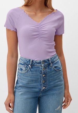 Helles lila geripptes Oberteil mit kurzen, gewellten Ärmeln und einem V-Ausschnitt, mit Raffung in der Mitte. Kombiniert mit hochgeschnittenen blauen Jeans.