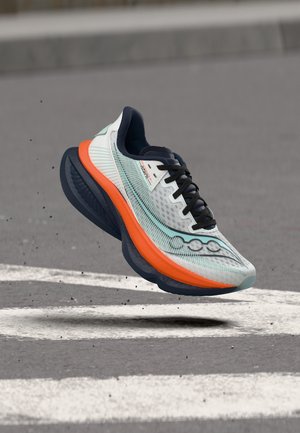 Αθλητικό παπούτσι σε ανοιχτό μπλε και πορτοκαλί με μαύρα κορδόνια αιωρείται πάνω από άσφαλτο με άσπρες οδικές σημάνσεις και μικρά μαύρα θραύσματα.