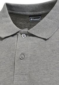 Nahaufnahme eines hellgrauen Poloshirt-Kragens mit zwei Knöpfen und einem schwarzen Etikett mit dem hummel-Markenlogo.