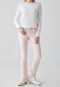 Top blanco de manga larga combinado con jeans rosa pálido. Los jeans cuentan con bolsillos frontales y un corte ajustado. Zapatillas blancas completan el conjunto.