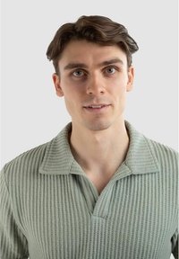 Ljusgrön ribbad pullover med krage, som har ett texturerat tyg och en avslappnad passform. Inga mönster eller dekorationer synliga.