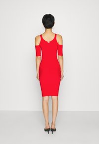 Robe bodycon rouge côtelée avec des manches dénudées. Longueur midi, silhouette ajustée, texture lisse et détail d'ouverture à l'arrière.