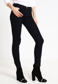 Mörkblå tajta jeans av denim med hög midja och en slät yta, kombinerade med svarta fotkängor med vit tåhätta.