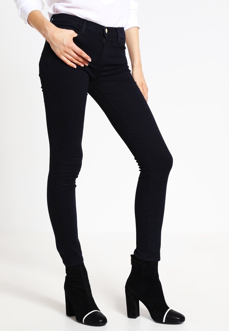 Mörkblå tajta jeans av denim med hög midja och en slät yta, kombinerade med svarta fotkängor med vit tåhätta.