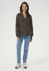 Blouse noire à manches longues avec un petit motif de feuilles multicolores. Associée à un jeans bleu clair et des baskets blanches. Coupe décontractée.
