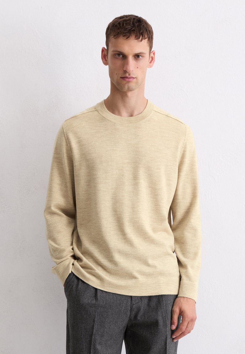 Beige Pullover mit langen Ärmeln und Rundhalsausschnitt, mit glatter Textur. Kombiniert mit dunkelgrauen, maßgeschneiderten Hosen. Einfaches und klassisches Design.