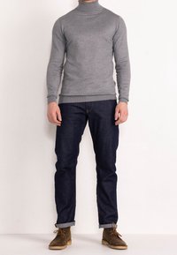 Pull col roulé gris de style ajusté, associé à un jean bleu foncé et des bottes en daim marron. Design simple, texture lisse et poignets retroussés.