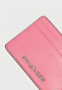 Ροζ δερμάτινη θήκη καρτών με υφή, που διαθέτει πολλαπλές θήκες και μεταλλικό ασημί λογότυπο "MICHAEL KORS".
