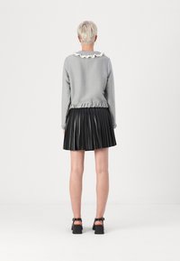 Pull en maille texturée gris avec un col en dentelle blanc, associé à une jupe plissée noire et des chaussures à talons blocs noires.